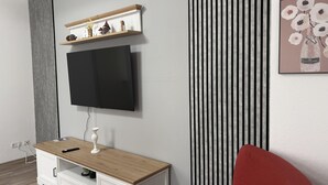 Ein modernes Wohnzimmer mit Flachbildfernseher an der Wand, einem Holztisch mit Lampe und einem roten Sessel.