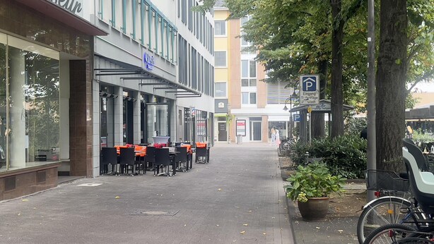 Eine Straße mit Außenbestuhlung, ein Gebäude mit der Aufschrift 'Schnapfer' und ein Parkschild.