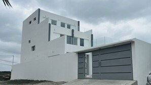 Un edificio moderno de dos pisos con fachada blanca, grandes puertas de garaje y una rampa de concreto que lleva a la entrada.