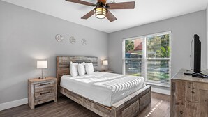A bedroom with a wooden bed, bedside tables, a ceiling fan, and a window with blinds. - Purple Paradise (Pensacola)