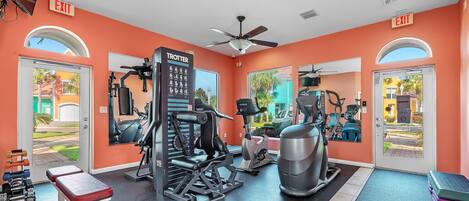 Un gimnasio con paredes anaranjadas, ventiladores de techo y diverso equipamiento de ejercicio.