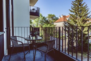 Een balkon met twee rieten stoelen en een kleine ronde tafel, met uitzicht op een woonwijk met bomen en huizen.