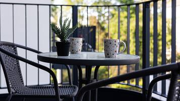 Une table ronde avec deux tasses décorées et une plante en pot, sur un balcon agrémenté de chaises en osier.