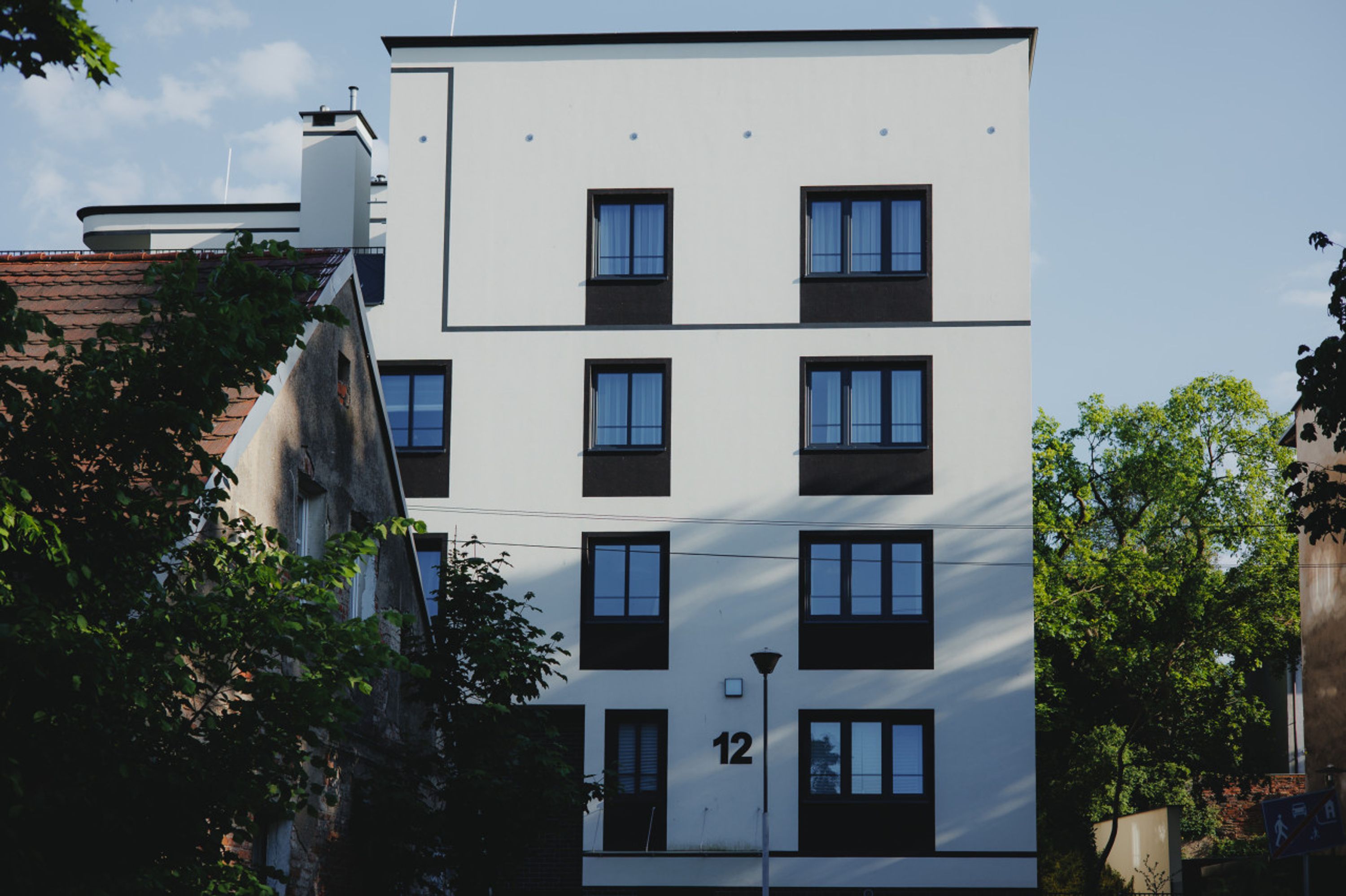 A modern multi-story building with a white facade, numbered 12, featuring evenly spaced windows and a flat roof.