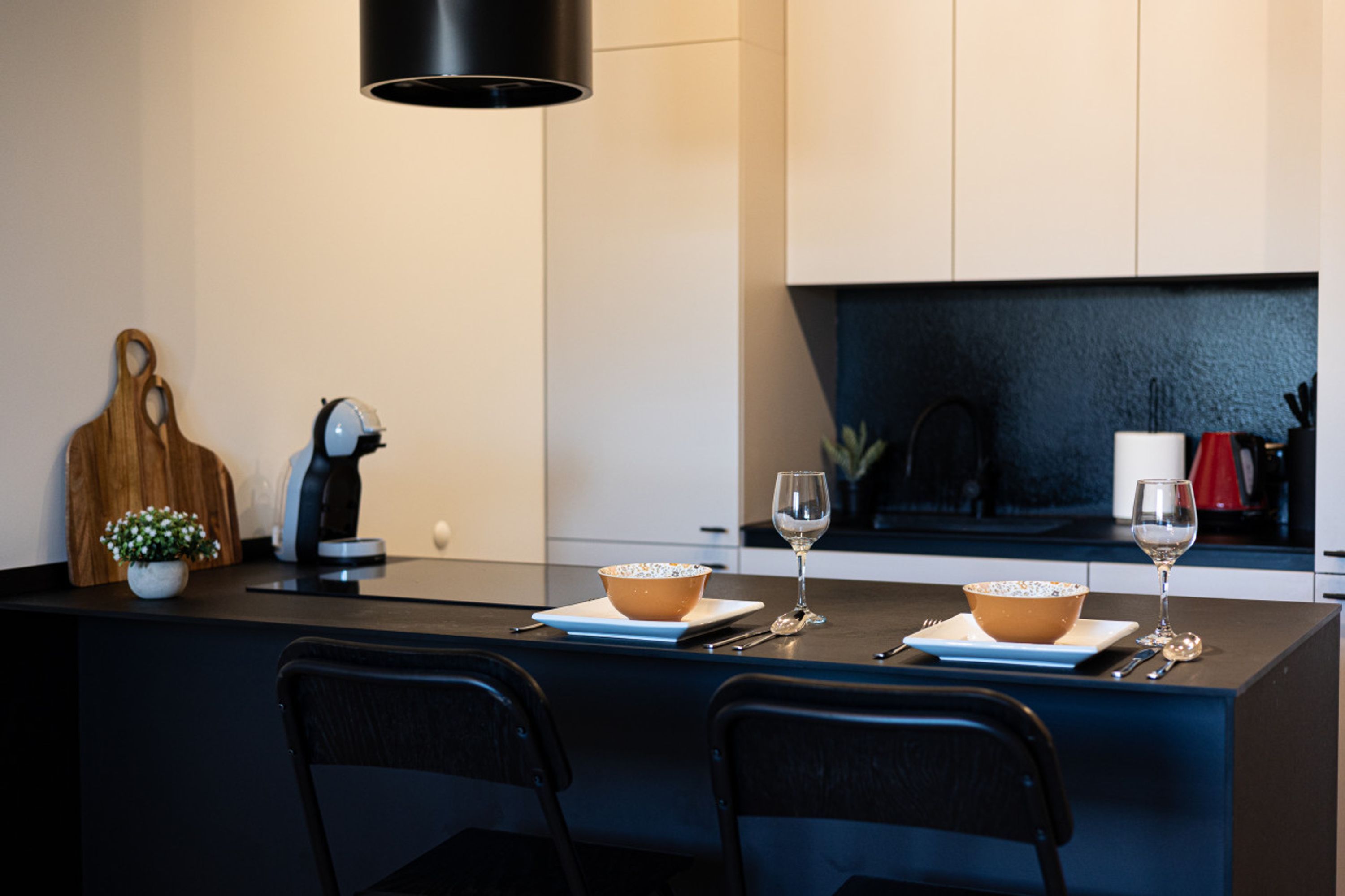 A modern kitchen with a central island, two chairs, a bowl, a wine glass, and a coffee maker.