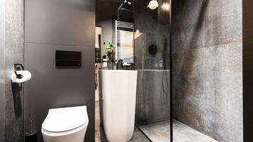 A modern bathroom with a toilet, a large mirror, a shower, and a glass-enclosed shower area.