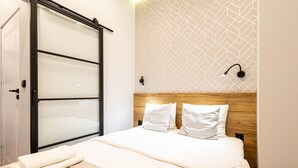 Une chambre d’hôtel moderne dotée d’un grand lit, d’une tête de lit en bois, d’un mur orné d’un motif géométrique et d’une porte coulissante.