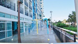 Un'area giochi con acqua, una palma, una struttura giallo e blu e un edificio con balconi e finestre.