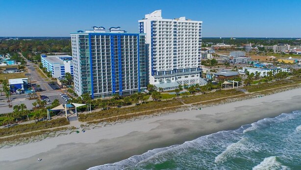 Un hotel sul lungomare con due edifici principali, un'area parcheggio e una spiaggia.