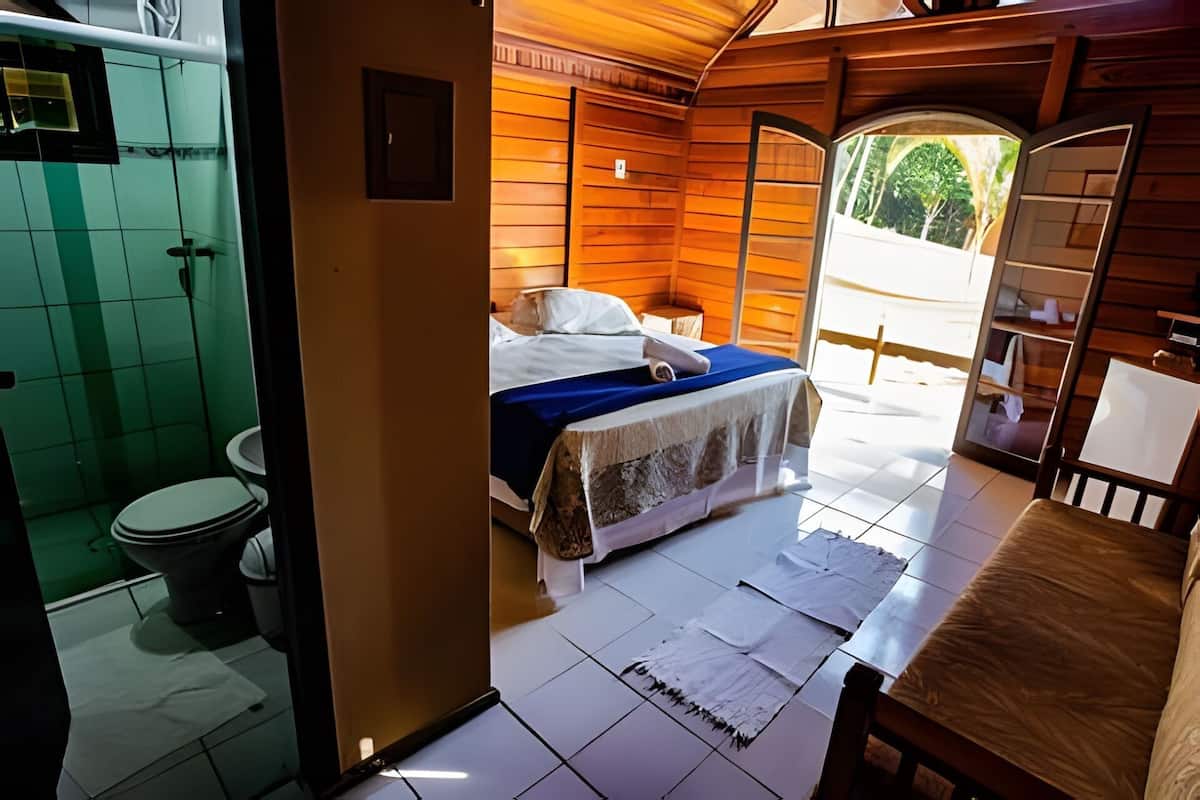 A wooden cabin-style room with a bed, a small table, and a view of the outdoors.