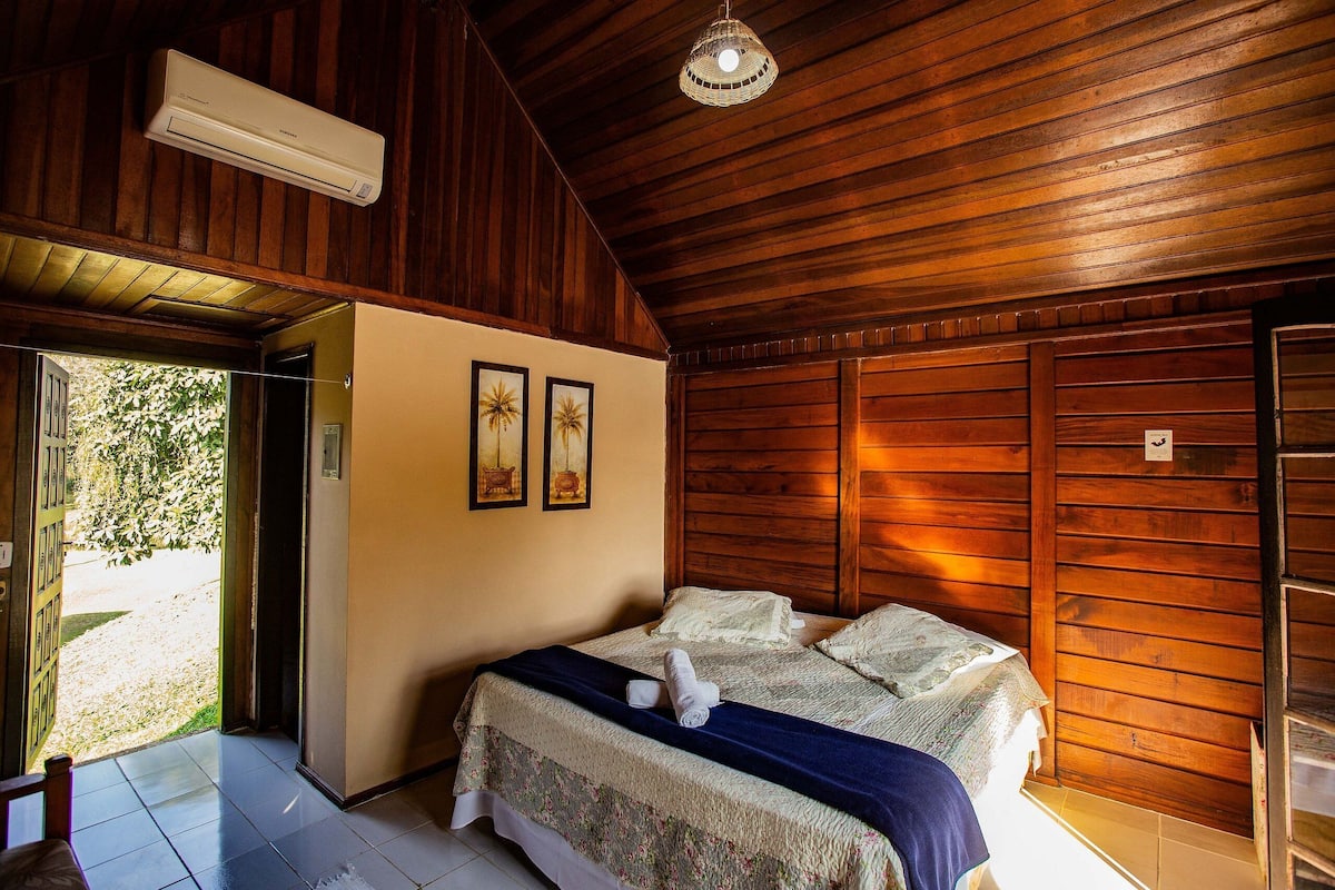 A room with a bed, wooden walls, a ceiling fan, and a door leading outside.