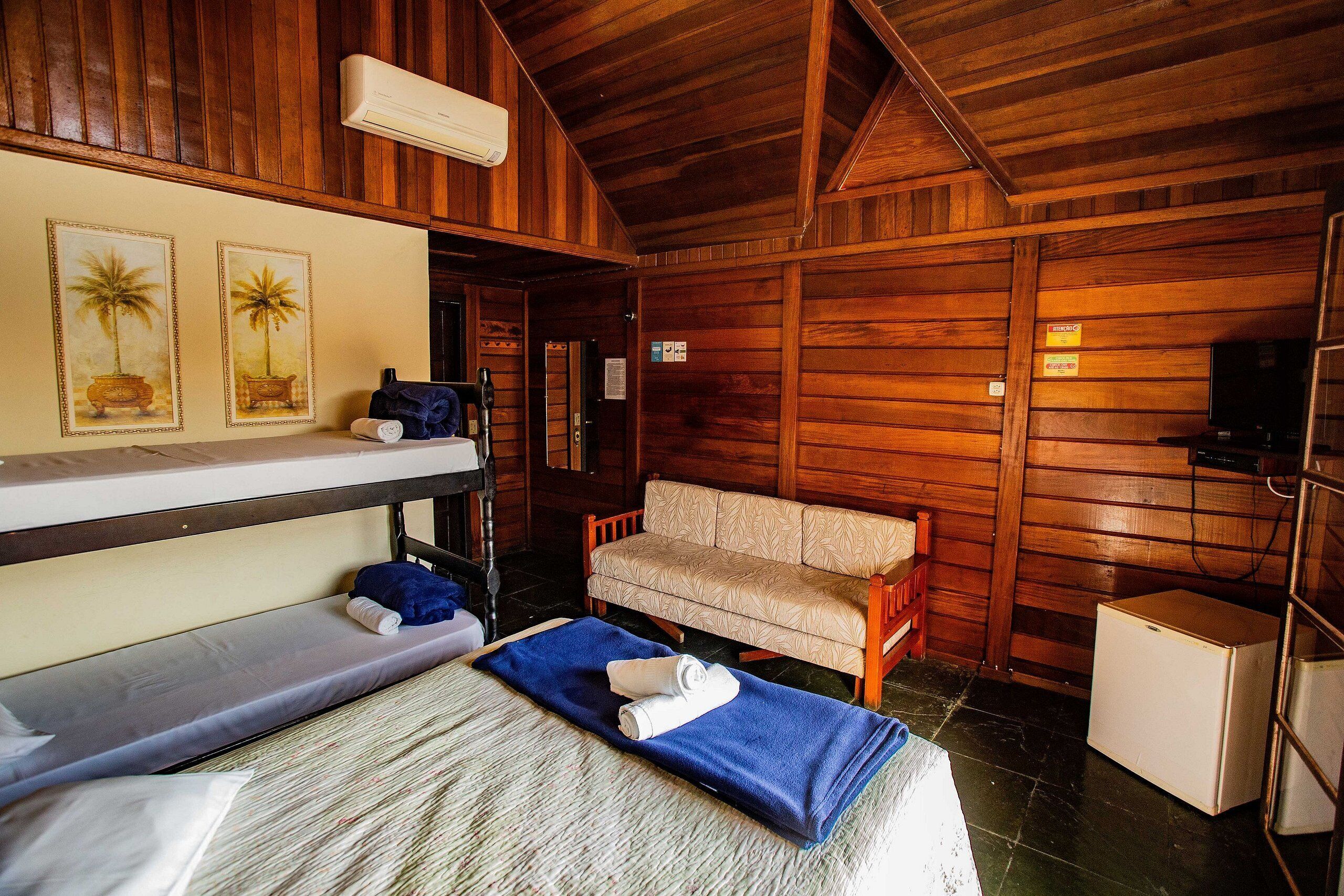 A wooden cabin room with bunk beds, a sofa, a small refrigerator, and wall-mounted air conditioning.