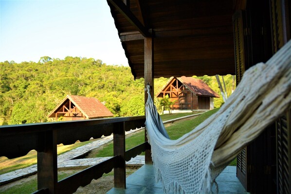 A hammock on a wooden deck overlooking a forested area with rustic cabins. - Recanto das Águas (Eldorado)