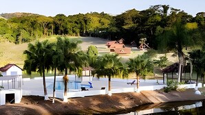 A serene landscape with a swimming pool, palm trees, and a small building. - Recanto das Águas (Eldorado)