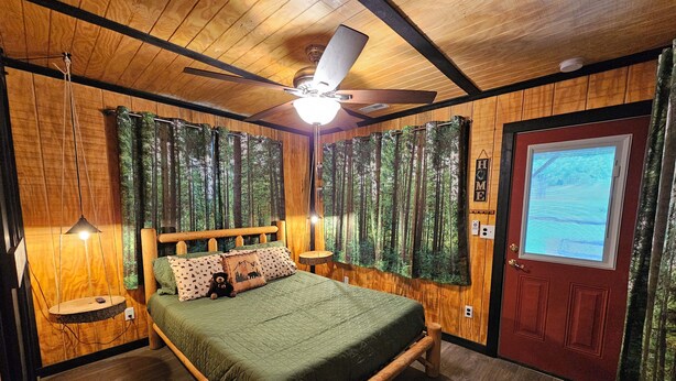 Un dormitorio de madera con una cama, un ventilador de techo y una puerta con ventanal.
