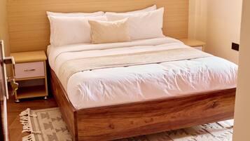 A neatly made bed with a wooden frame and white bedding, a bedside table with a lamp, and a patterned rug on the floor.
