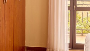 Ein Schlafzimmer mit einem Holzschrank, einer Schiebetür zum Balkon und einem weißen Vorhang.