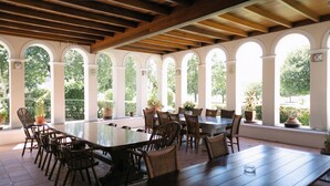 A covered patio with a long table and chairs, surrounded by arched windows with potted plants. - Manor House at La Roche Estate - Franschhoek (Franschhoek)