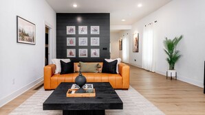 Una sala de estar moderna con una mesa de centro negra, sofá de cuero naranja y obras de arte enmarcadas en la pared.