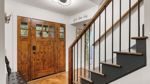 A wooden double door with glass panels, a black staircase with wooden handrails, and a wall with a sign that reads "Good Things Only".