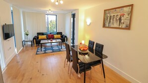 A modern living room with a dining area, featuring a sofa, coffee table, and a painting on the wall.