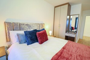Un lit bien fait, avec une literie blanche et rouge, une tête de lit en bois et une table de chevet avec une lampe.