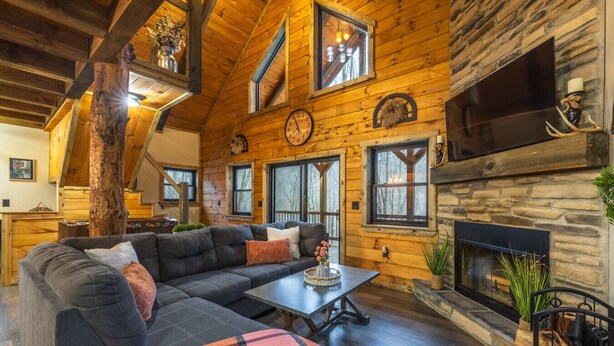 A log cabin interior with a sectional sofa, a fireplace, wooden walls, and a stone accent wall. - New Amish built cabin opening up March 14, 2025 near Hocking Hills/Tar Hollow St.Forest (Londonderry)