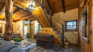 A cozy cabin interior with a wooden ceiling, a foosball table, a sofa, and a staircase. - New Amish built cabin opening up March 14, 2025 near Hocking Hills/Tar Hollow St.Forest (Londonderry)