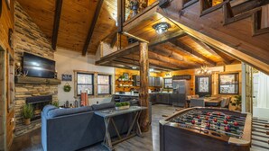 A cozy loft-style living area with a sofa, a foosball table, and a kitchen in the background. - New Amish built cabin opening up March 14, 2025 near Hocking Hills/Tar Hollow St.Forest (Londonderry)
