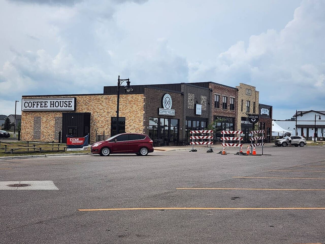 A coffee house with a brick facade, a red car parked in front, and construction barriers.