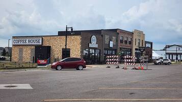 A coffee house with a brick facade, a red car parked in front, and construction barriers.