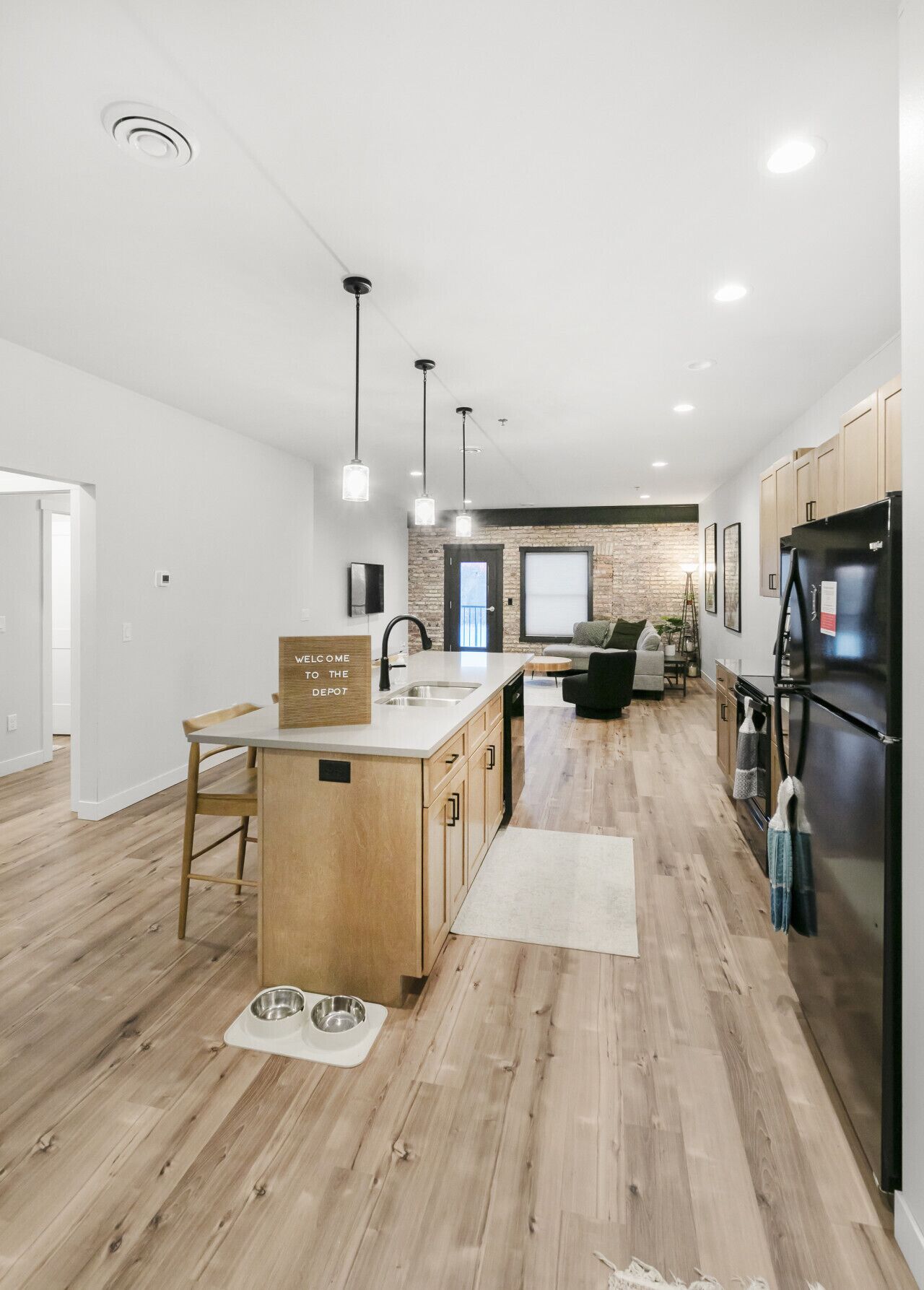 A modern kitchen with wooden flooring, a central island, and a black refrigerator.