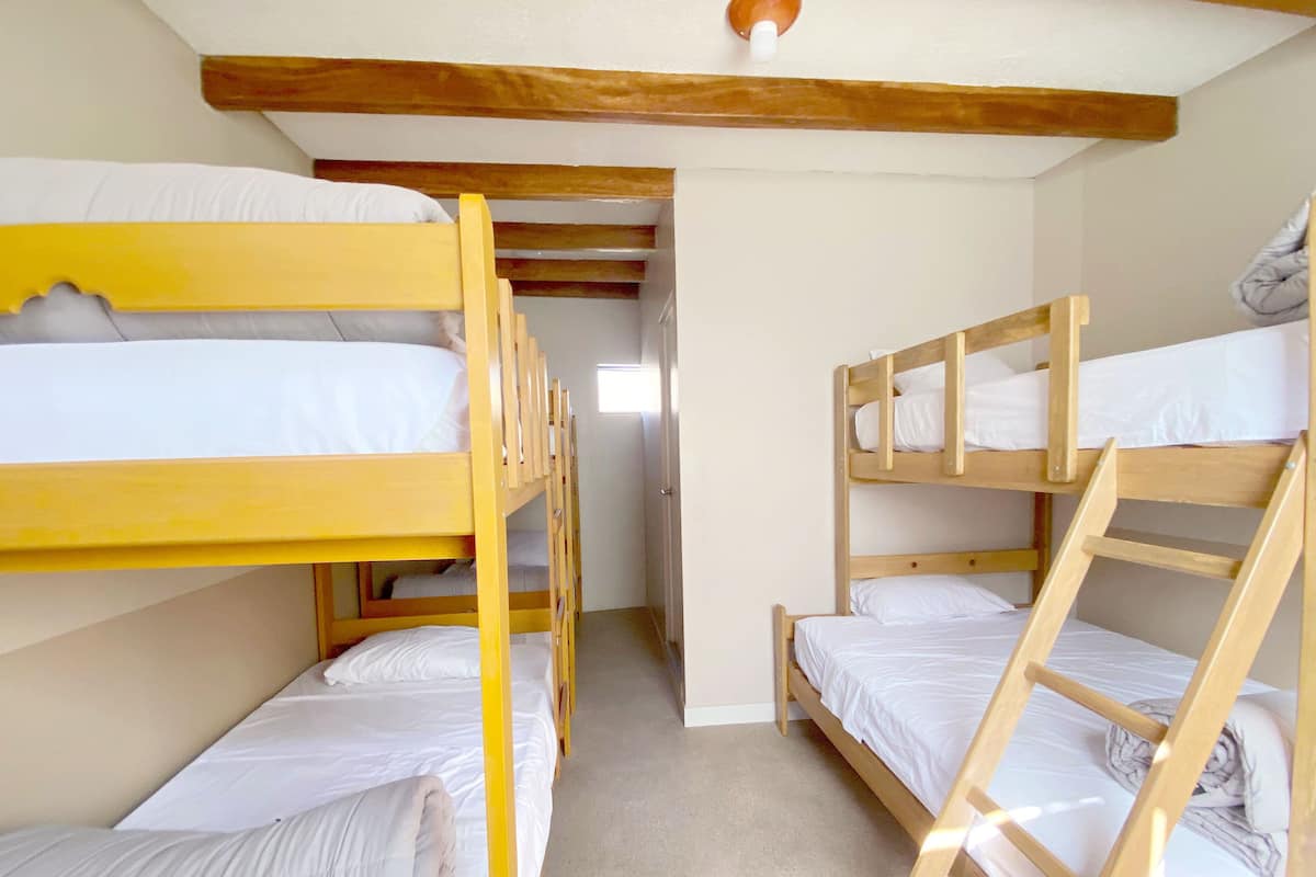 A room with bunk beds, wooden beams, and a door leading to another room.