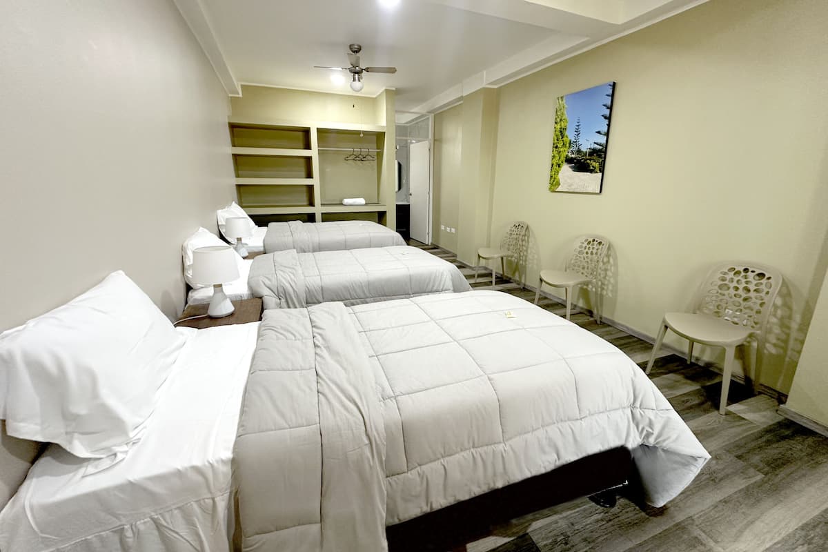 A hotel room with two beds, a ceiling fan, a small table, two chairs, and a painting on the wall.