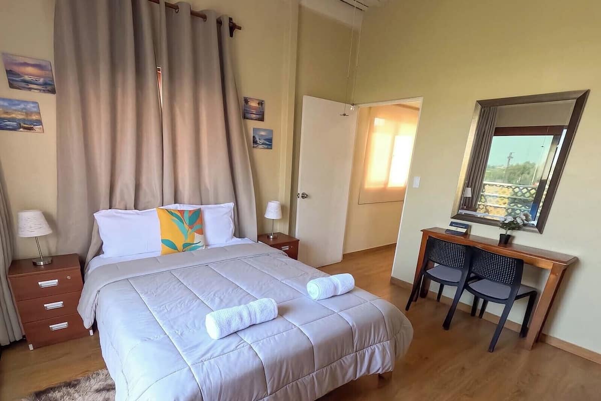 A hotel room with a bed, a desk, a chair, a mirror, and a door.