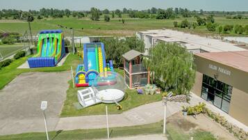 Un patio de juegos al aire libre con toboganes y estructuras inflables, una cancha de tenis y un edificio con el rótulo 'SALON PARAISO'.
