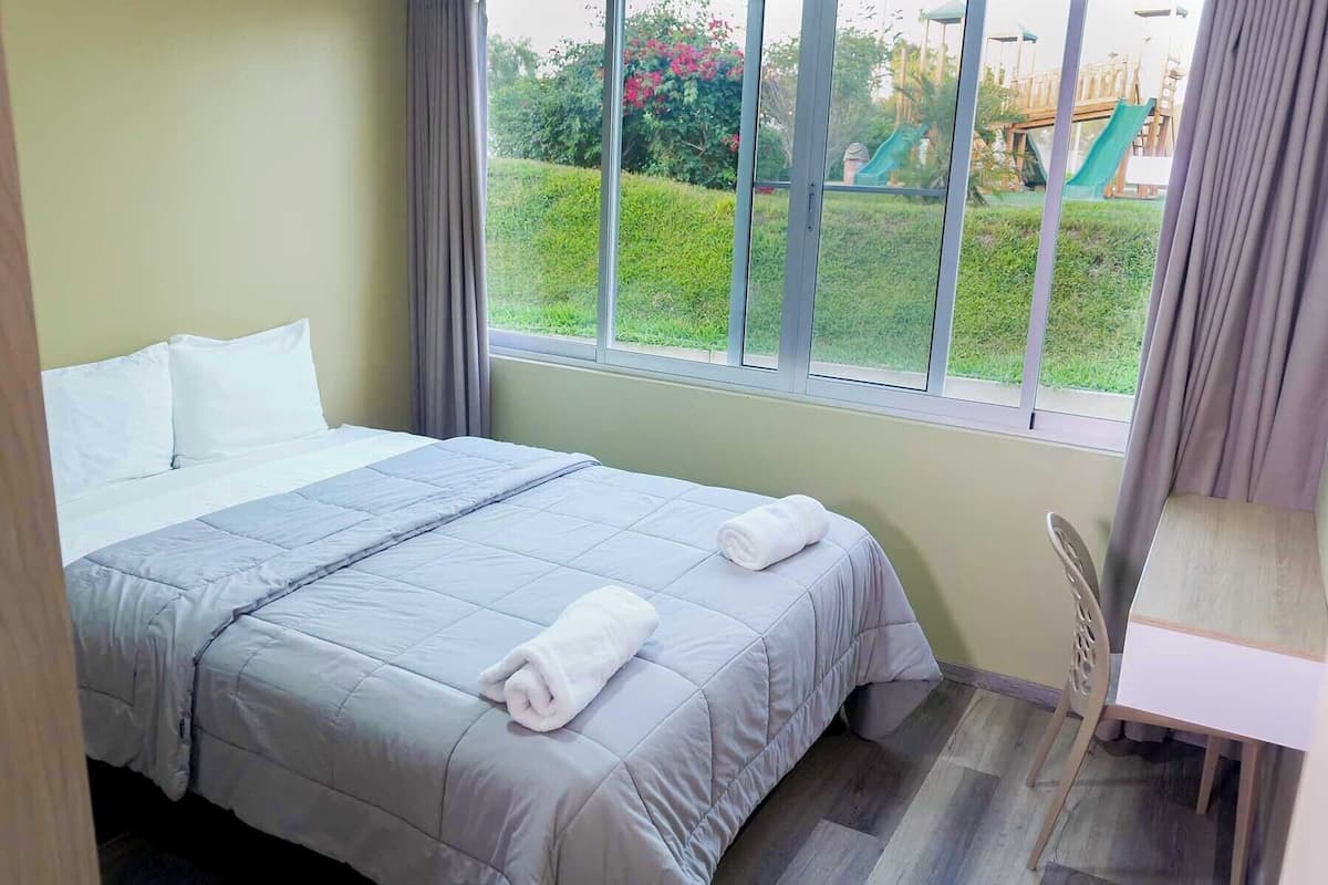 A hotel room with a bed, a window with a view of a playground, and a desk with a chair.
