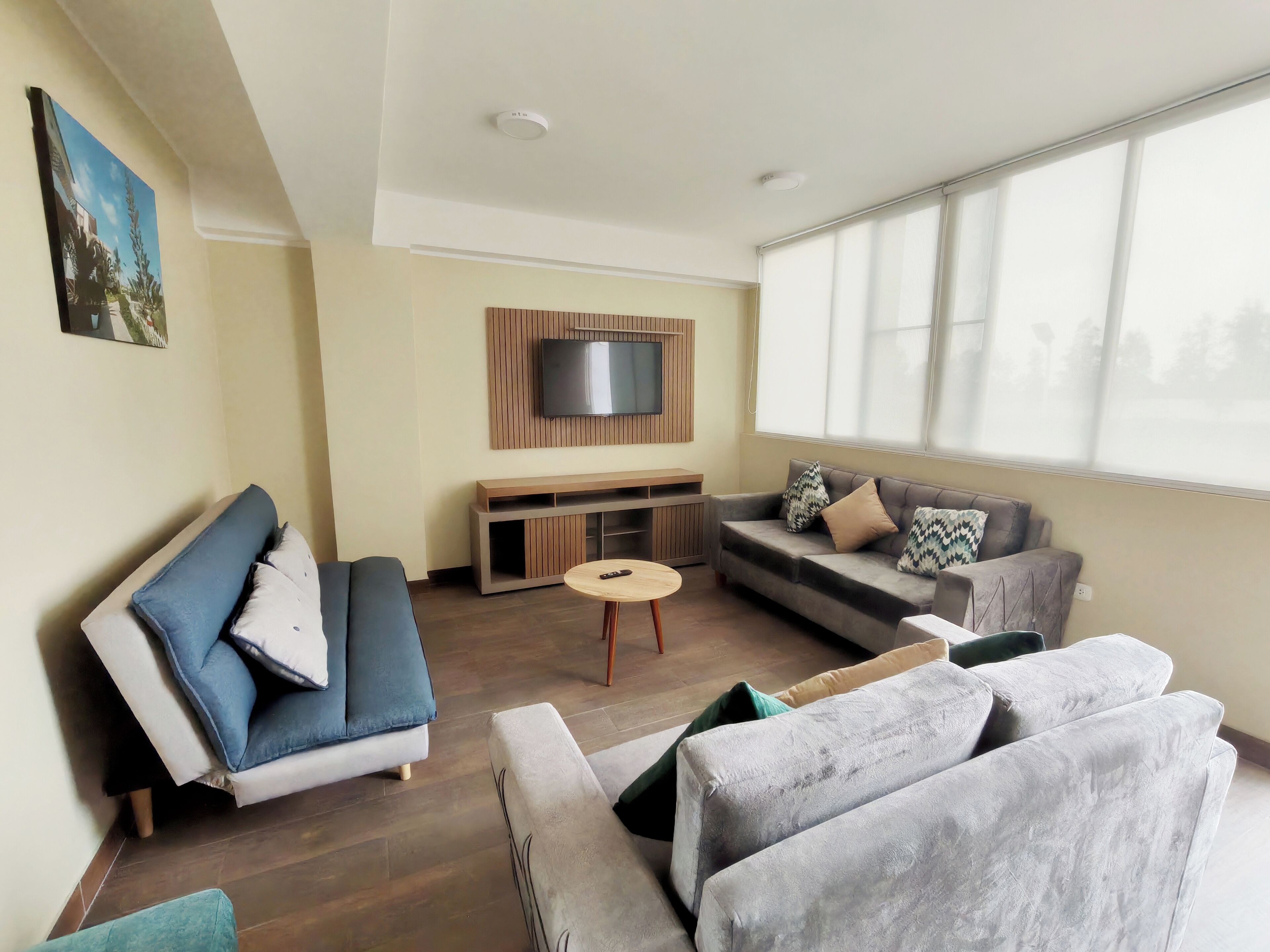 Una sala de estar moderna con un sofá, un sillón, una mesa de centro y un televisor montado en una pared de paneles de madera.
