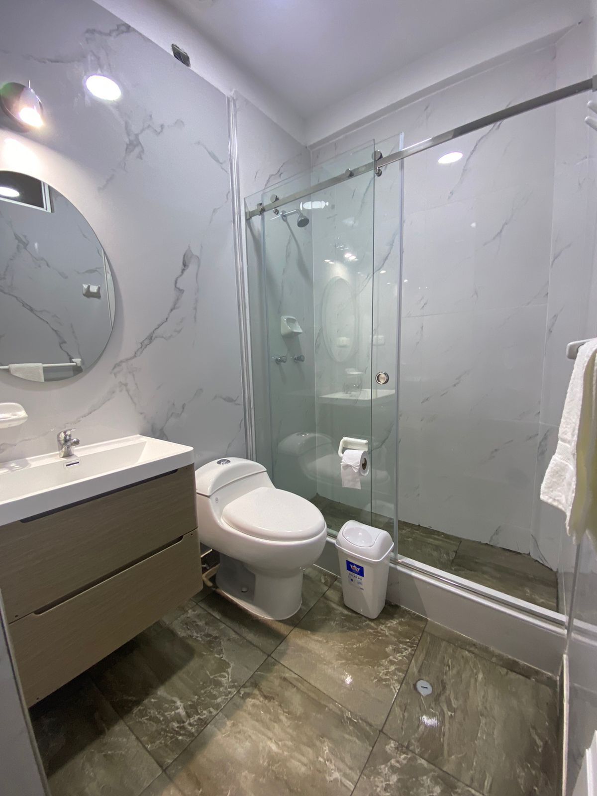 Un baño moderno con pared de mármol, cabina de ducha de vidrio, inodoro y lavamanos con espejo.