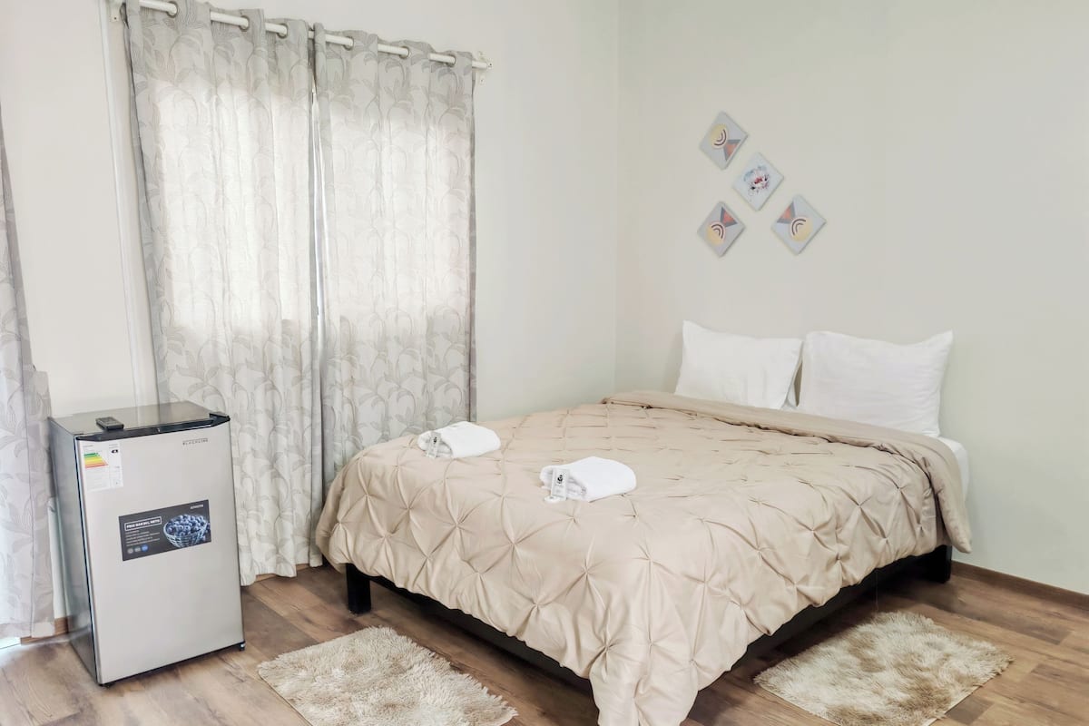 A hotel room with a bed, a refrigerator, a window with curtains, and a wall with pictures.