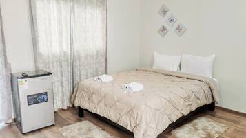 Una habitación de hotel con cama, refrigerador, ventana con cortinas y un cuadro en la pared.