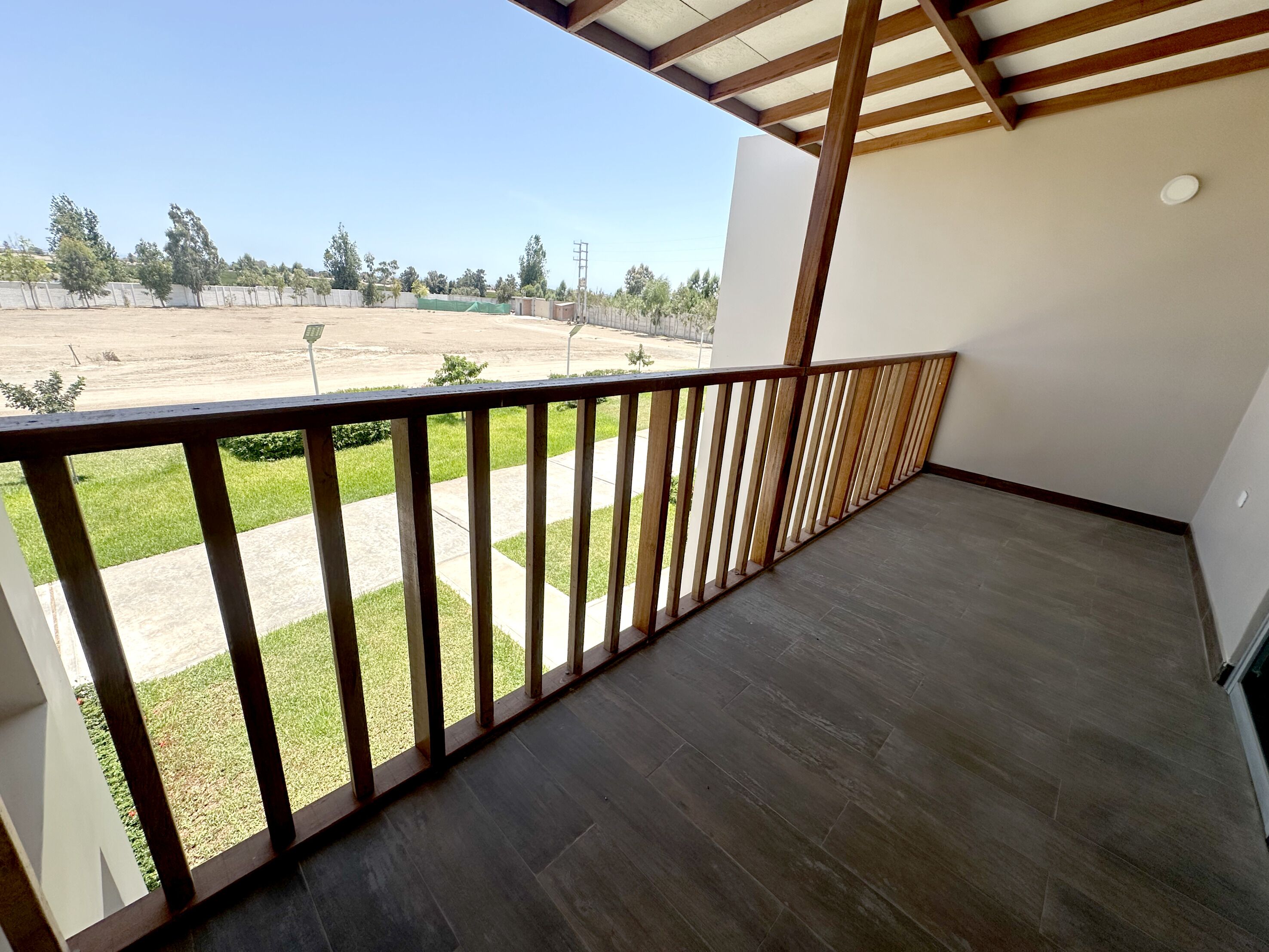 A balcony with a wooden railing overlooking a grassy area and a paved path.