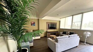 A modern living room with a large potted plant, a grey sofa, a small round table, and a flat-screen TV mounted on the wall. - EL PARAISO ECO RESORT (San Andrés)