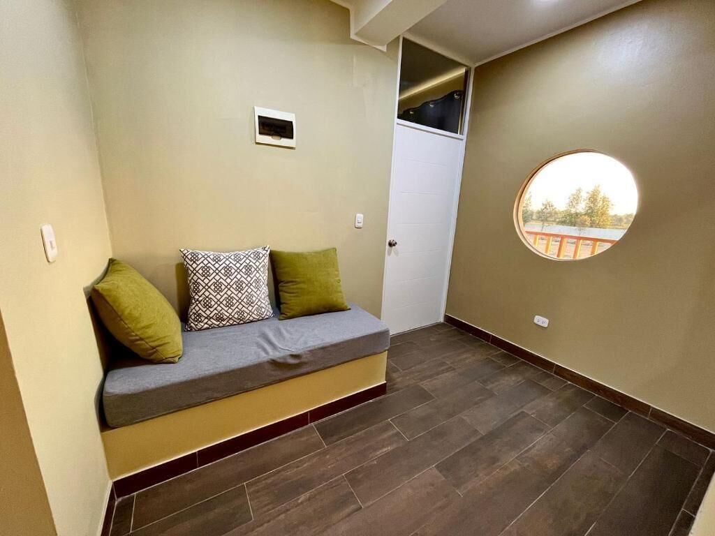 A room with a built-in bench, a door, a small window, and a round mirror on the wall.