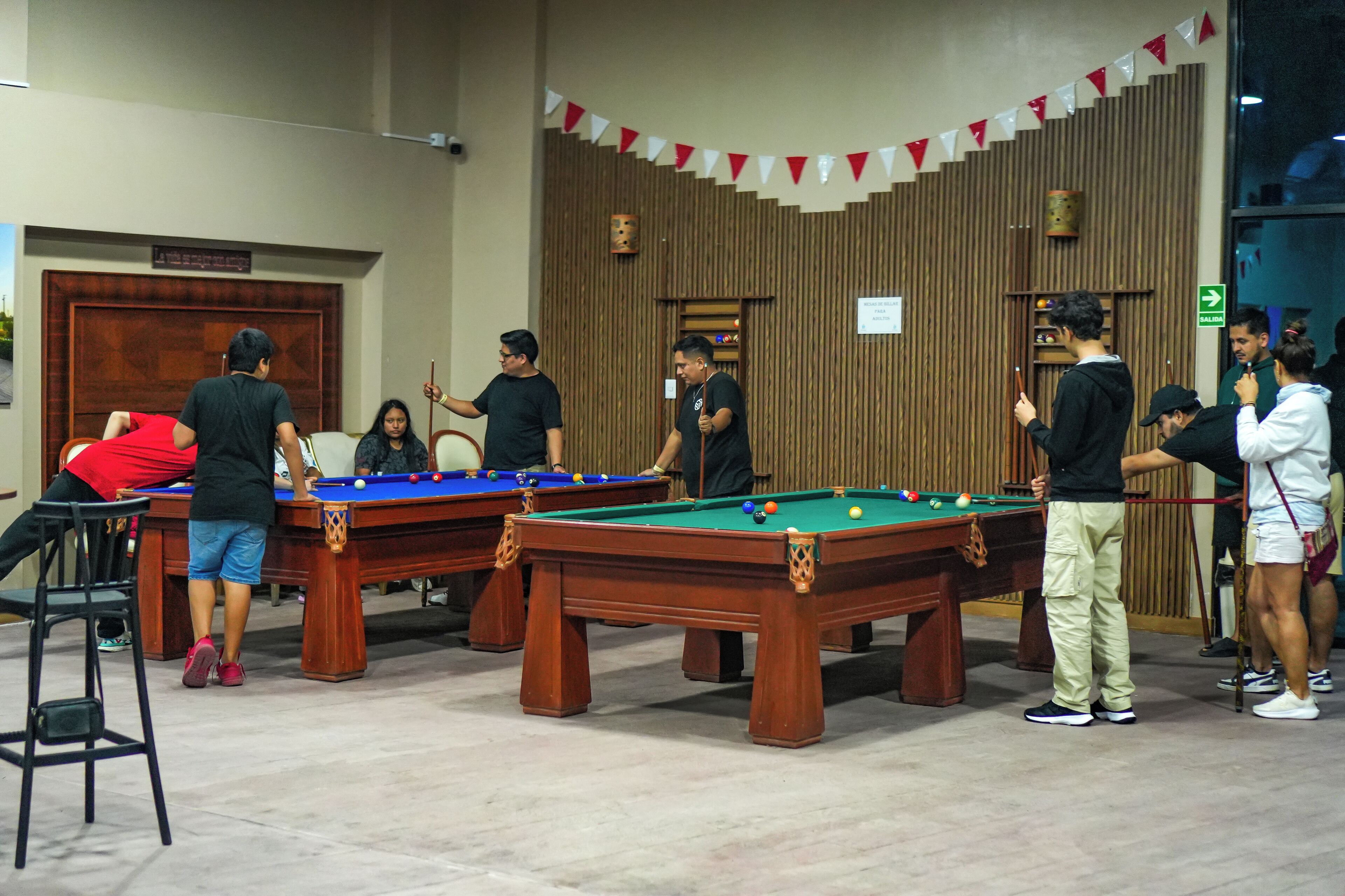 A pool hall with multiple pool tables, wooden walls, and a red and white banner.