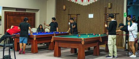 A pool hall with multiple pool tables, wooden walls, and a red and white banner.
