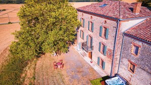 A rustic stone building with a large tree in front, a hot tub, and a small outdoor seating area. - Casa Lounell Swimming pool-SPA-Sauna-Games room, panoramic view   (Graulhet)