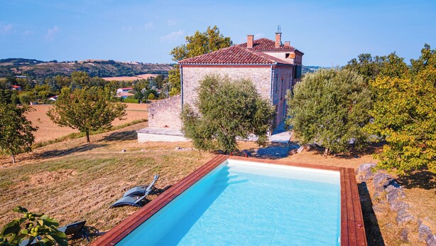 A rectangular swimming pool with a wooden deck, surrounded by trees and a stone building with a tiled roof. - Casa Lounell Swimming pool-SPA-Sauna-Games room, panoramic view   (Graulhet)