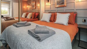 Una habitació d'hotel amb un llit gran, dos llits més petits, un mirall i una pintura al mur.