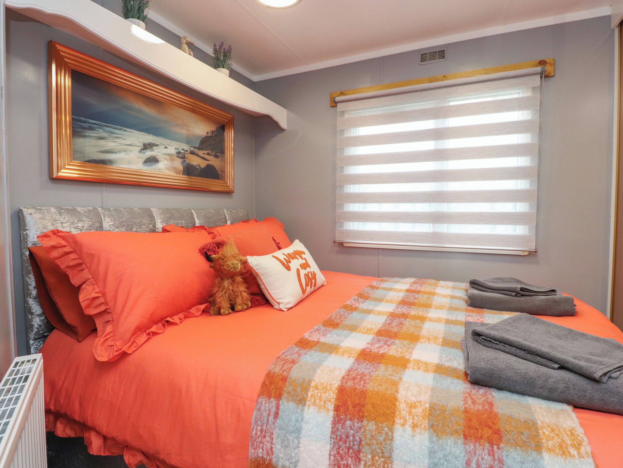 A bedroom with a bed, pillows, a blanket, a painting, a window with blinds, and a radiator.